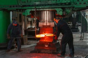 Two men heat metal in a manufacturing facility
